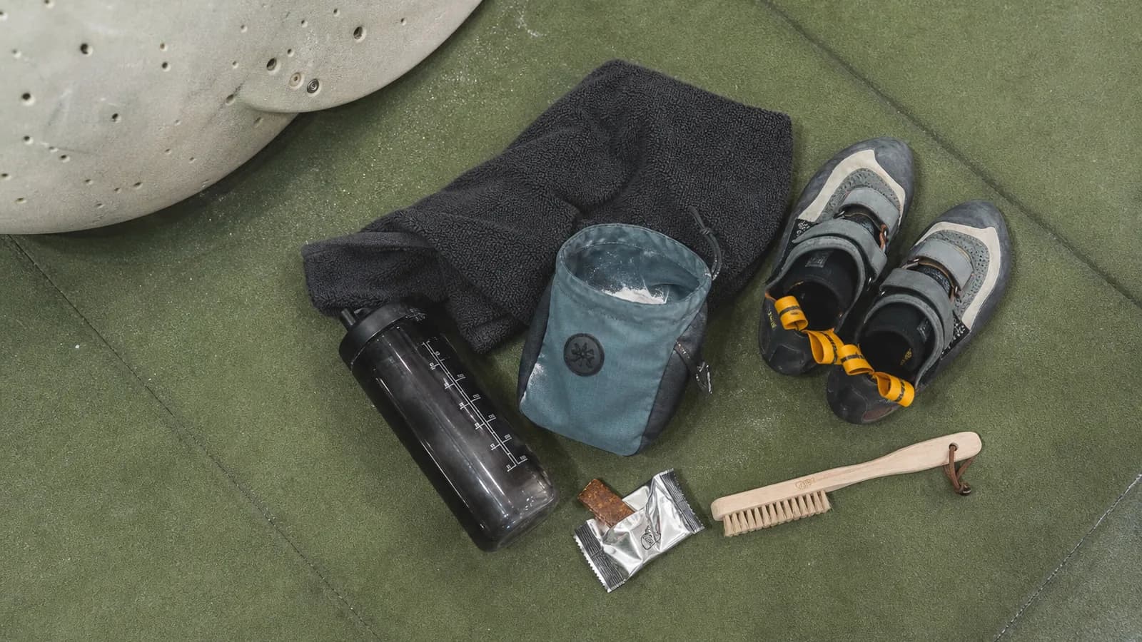 Crashpad noir et orange déplié au pied d'un bloc de grès patiné à Fontainebleau, chaussons de grimpe La Sportiva et sac à magnésie posés dessus, lumière de fin d'après-midi entre les arbres